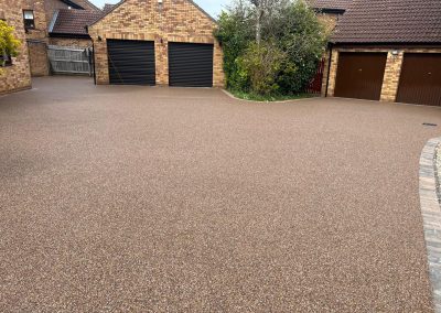 Spacious light brown resin bound driveway surrounded by brick houses.