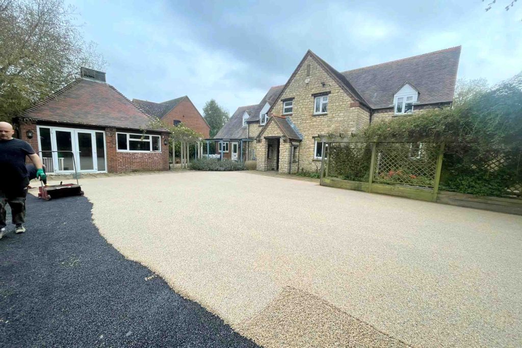 Resin bound driveway being installed beside a large stone house.