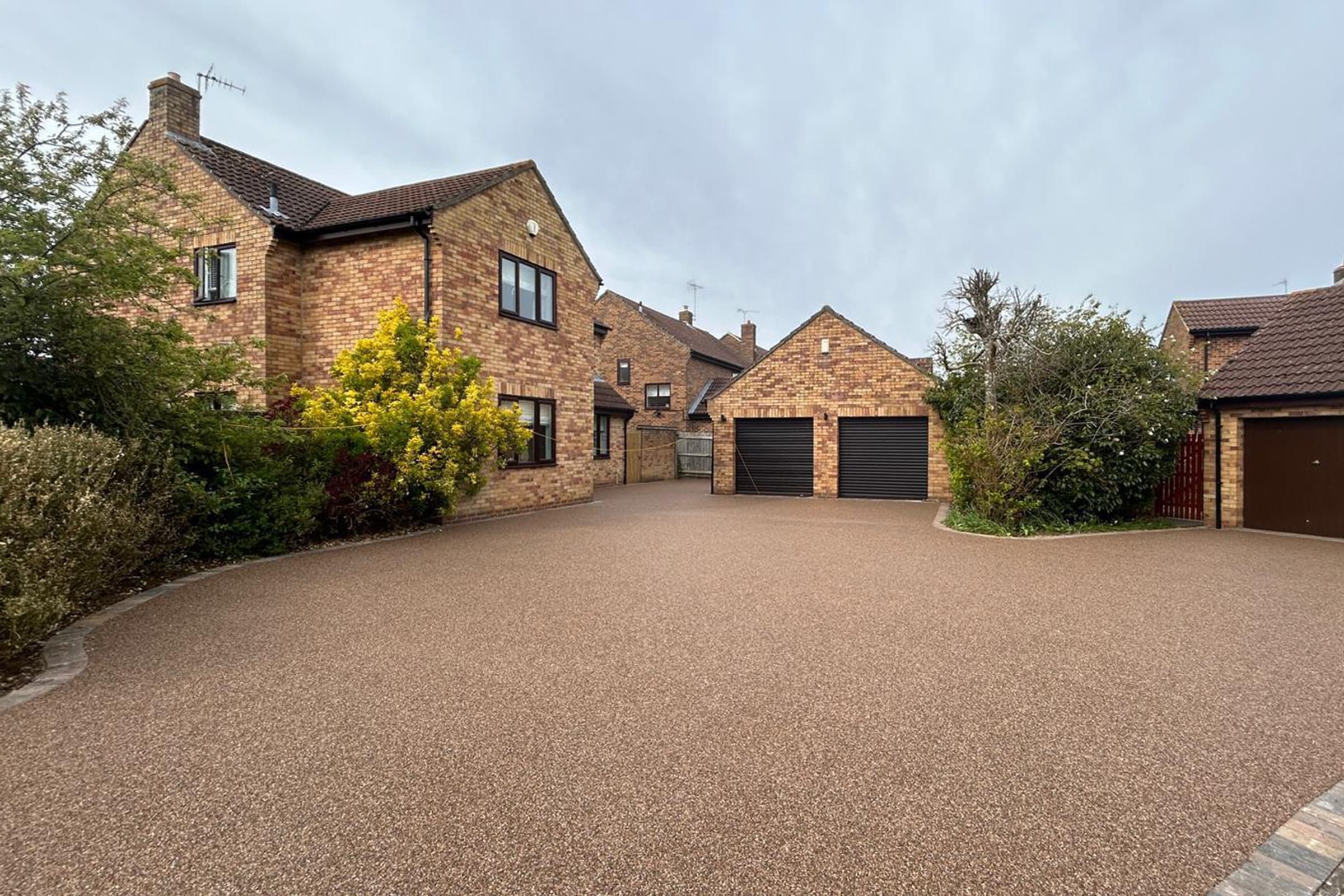 Spacious light brown resin bound driveway surrounded by brick houses.